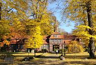 1611_1730 Die Herbstsonne scheint auf die Herbstbume, die beim historischen Torhaus von Hamburg Wellingsbtel stehen. Der Rasen vor dem historischen Gebude ist mit gelben Blttern bedeckt; ein Passant geht auf dem Kopfsteinpflaster zum Fachwerkgebude des 1757 errichteten Torhauses. 