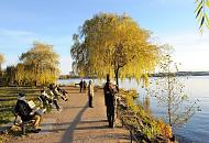 460_1343  Die HamburgerInnen geniessen die Herbstsonne auf Parkbnken am Ufer der Alster oder blicken vom Weg auf die untergehende Sonne - die Bltter der Weiden am Rand des Wassers sind gelblich, herbstlich gefrbt.  