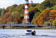 912_1730  Ein Tuckerboot fhrt auf der Elbe Hhe Leuchtfeuer Wittenbergen - auf der Wassertreppe, die zum Anleger fhrt stehen Spaziergnger und blicken auf die Elbe. Die Bume am bewaldeten Ufer tragen teilweise Herbstfrbung.  