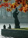 16_03816 zwei HamburgerInnen sitzen in der herbstlichen Abendsonne auf der Mauer am Ufer der Binnenalster; die Skulptur "Die Windsbraut" von Hans-Martin Ruwoldt wirft einen langen Schatten - davor das rotbraune und goldene Herbstlaub von einem Ahorn.  www.christoph-bellin.de