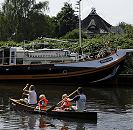 17_21585 Eine Familie paddeln in einem Kanu auf der Dove-Elbe - die Kinder tragen zur Sicherheit Schwimmwesten. Am Ufer liegt ein Segelschiff, das zum Hausboot umgebaut wurde, dahinter ein strohgedecktes Wohnhaus.  www.hamburg-fotograf.com