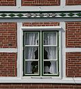 17_21631 Holzfenster in einem Fachwerkhaus; die Gardinen sind mit Spitzen versehen. Der Balken ber dem Fenster ist mit farbig abgesetzten Schnitzereien versehen. www.hamburg-fotograf.com