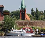 17_21647 Der Kirchturm der St. Nikolaikirche in Hamburg Moorfleet wurde 1885 errichtet. Im Vordergrund ein Sport- boot mit herunter geklapptem Verdeck und Bootsstege im Holzhafen; dahinter ist der Deich zu erkennen  www.hamburg-fotograf.com