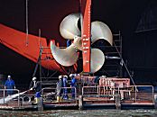 011_22118/00 im Trockendock der Schiffswerft Blohm + Voss bekommt ein Frachtschiff eine neue Schiffsschraube aus glnzendem Messing - Hafenarbeiter reinigen die Werftanlage  mit einem Wasserstrahl.