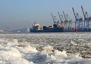 005_22734 Dichtes Treibeis auf der Elbe und am Ufer vor Hamburg Oevelgoenne. Das beladene britische Containerschiff Maike D. fhrt flussabwrts durch das Eis. Die Containerbrcken am Athabaskakai des Container Terminals Burchardkai sind hochgefahren - eine signalrote Tonne begrenzt die Fahrrinne fr die Schiffe auf der Elbe.