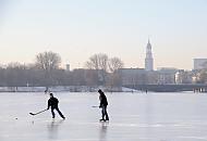 44_5574 Hamburger Jugendliche spielen Eishockey auf der zugefrorenen Alster - hinter der Kennedybrcke sind die Huser am Jungfernstieg zu erkennen und der Kirchturm der St. Michaeliskirche. Hamburger Jahreszeiten, die Hansestadt im Winter - Eishockeyspieler auf der Auenalster. 
