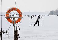 7_6093 Vor dem Anleger des Bootssteg vom Alstercaf Bobby Reich luft ein Hamburger Ski auf der zugefrorenen und verschneiten Alster; ein schneebedeckter Rettungsring hngt am Steg in seiner Halterung. Bilder vom Hamburger Winter - Langskilaufen auf der verschneiten Alster.