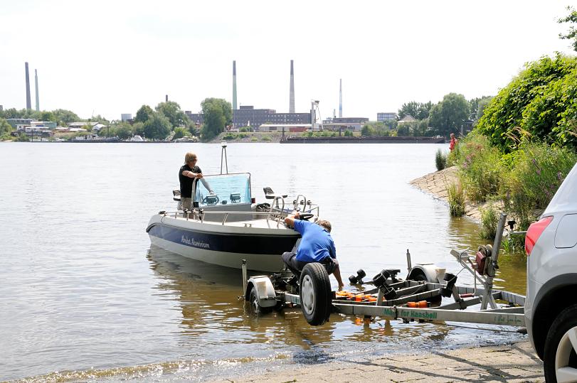 01173_3703 Ein Sportboot wird von einem Trailer auf der Slipanlage im Elbpark Entenwerder zu Wasser gelassen - auf der anderen Seite der Norderelbe Industrieschornsteine und Gebude auf der Peute in Hamburg Veddel.