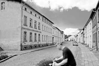 7655 Einstöckige Wohnblocks, Etagenwohnungen im Hansensgang von Pritzwalk - Fahrradfahrer in Fahrt, Schwarz-Weiss-Fotografie.